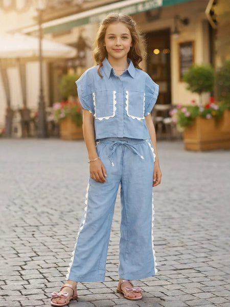 Young girl in a blue outfit standing on a cobblestone street.