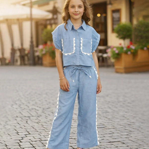 Young girl in a blue outfit standing on a cobblestone street.