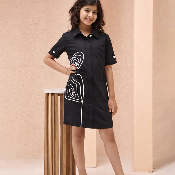 Young girl wearing a black dress with white patterns against a beige background
