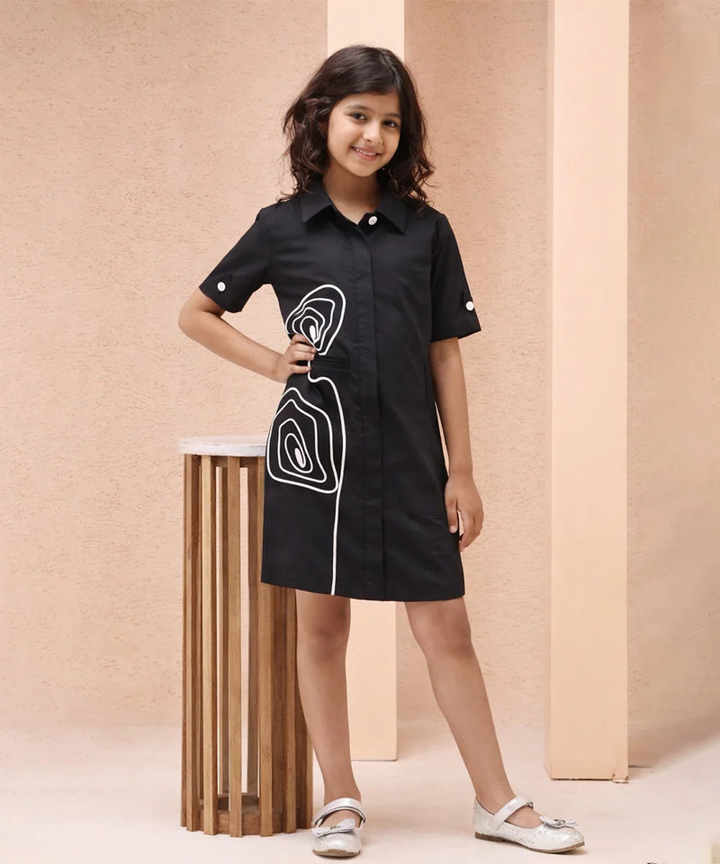 Young girl wearing a black dress with white patterns against a beige background