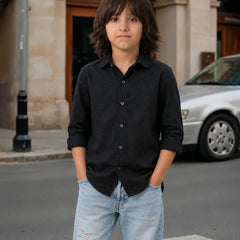 Young boy in a black shirt and light blue jeans standing on a street.