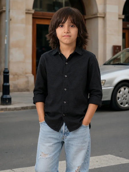Young boy in a black shirt and light blue jeans standing on a street.