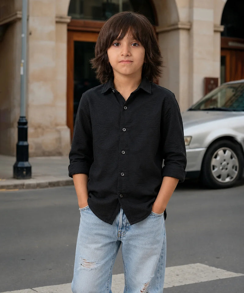 Young boy in a black shirt and light blue jeans standing on a street.