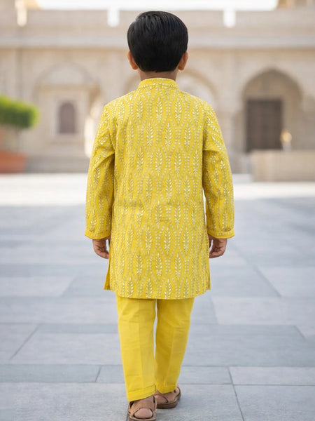 Child wearing a yellow traditional outfit standing in an outdoor setting with architectural elements.