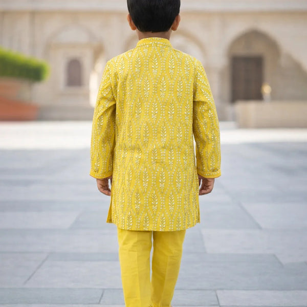 Child wearing a yellow traditional outfit standing in an outdoor setting with architectural elements.