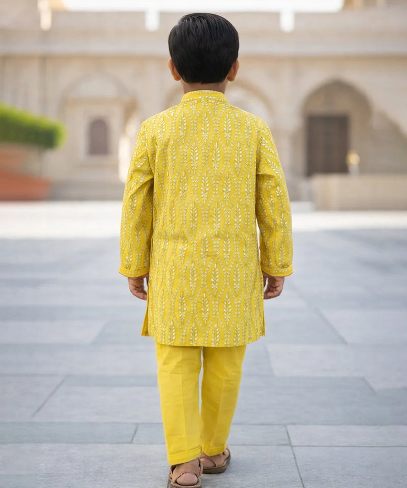 Child wearing a yellow traditional outfit standing in an outdoor setting with architectural elements.