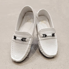 Pair of white loafers with decorative buckles on a beige background