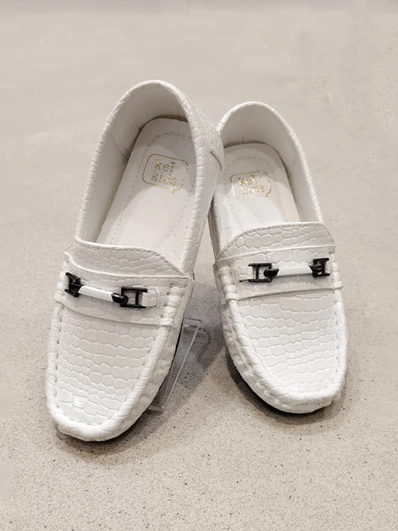 Pair of white loafers with decorative buckles on a beige background