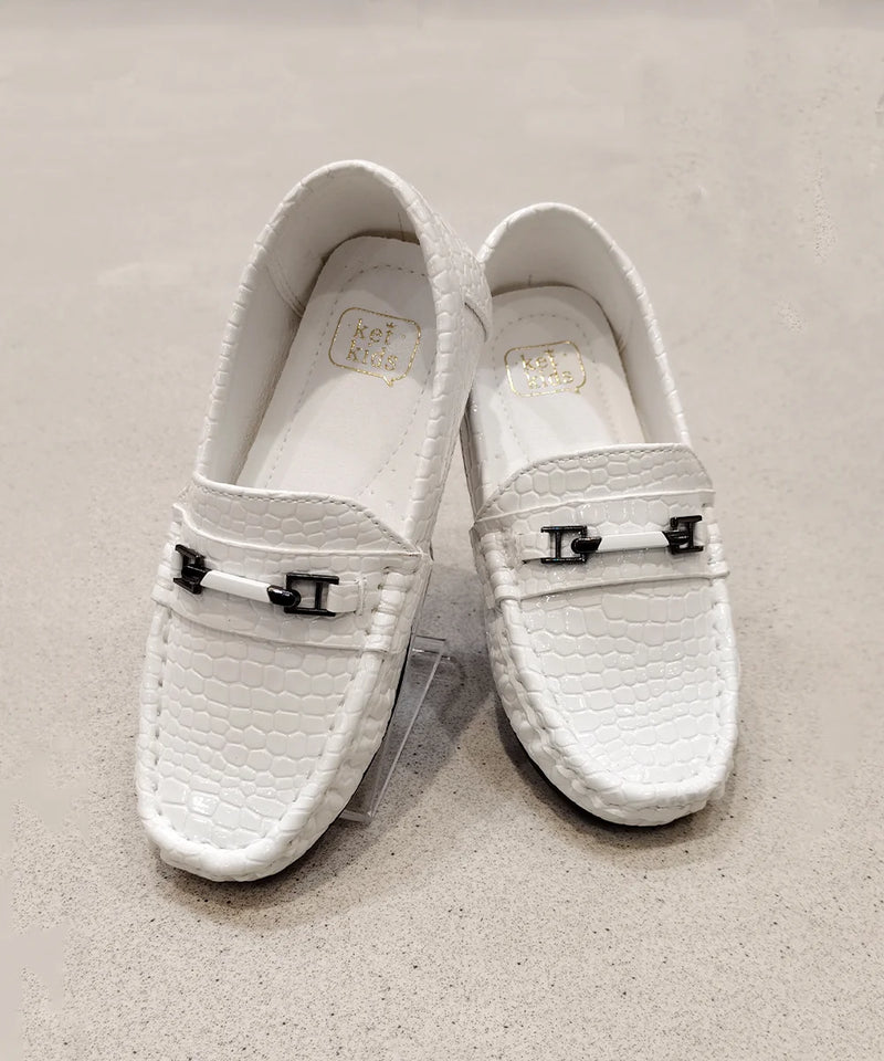 Pair of white loafers with decorative buckles on a beige background