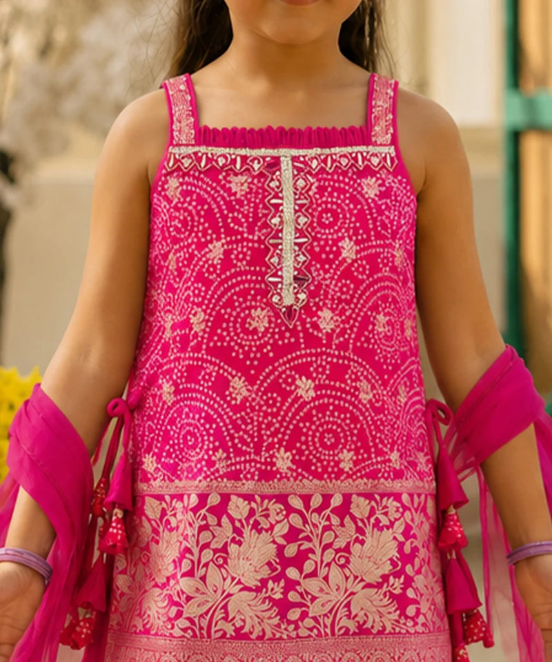 A close-up of a child wearing a bright pink sleeveless embroidered dress with beige floral and geometric patterns, paired with matching pink arm wraps.