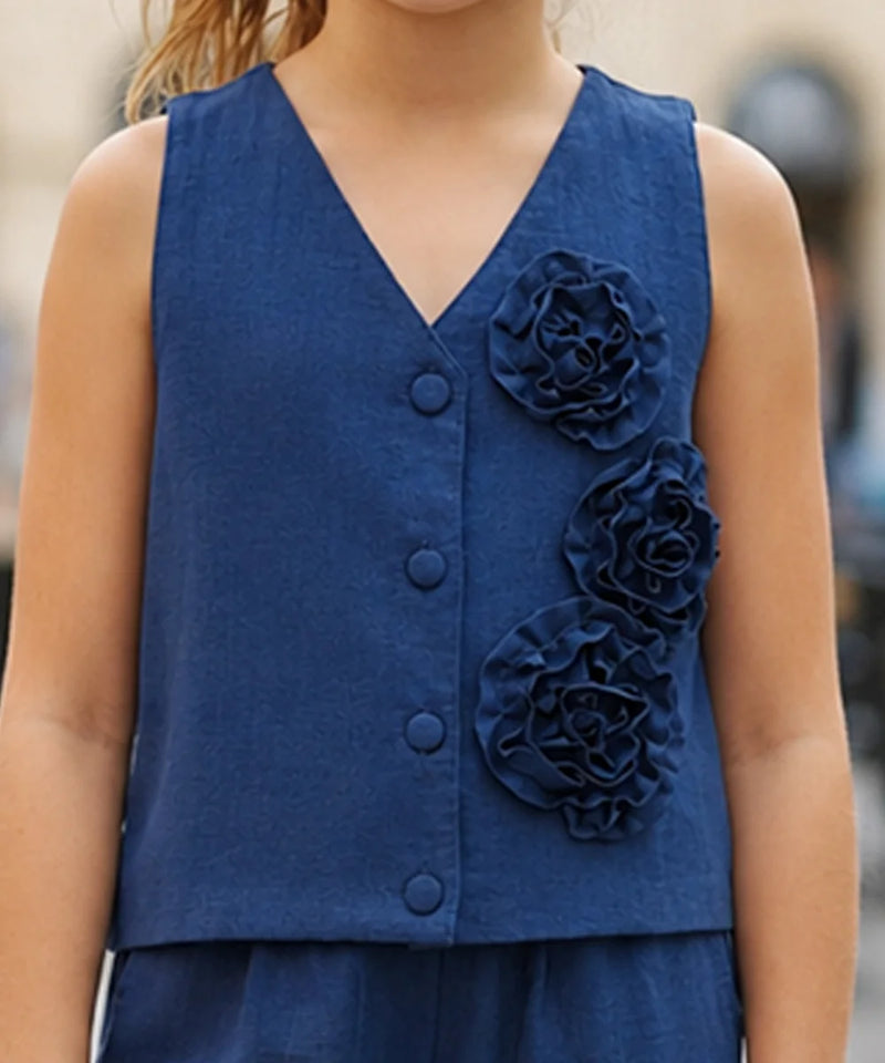 A sleeveless navy blue V-neck vest with three large fabric flowers on the front, worn by a child in an outdoor setting.