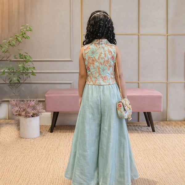Woman in a floral top and light blue skirt standing in a room with a pink bench and decorative wall.