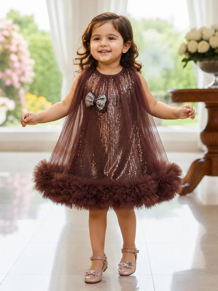 Young girl in a brown sequined dress with a fluffy skirt standing indoors.
