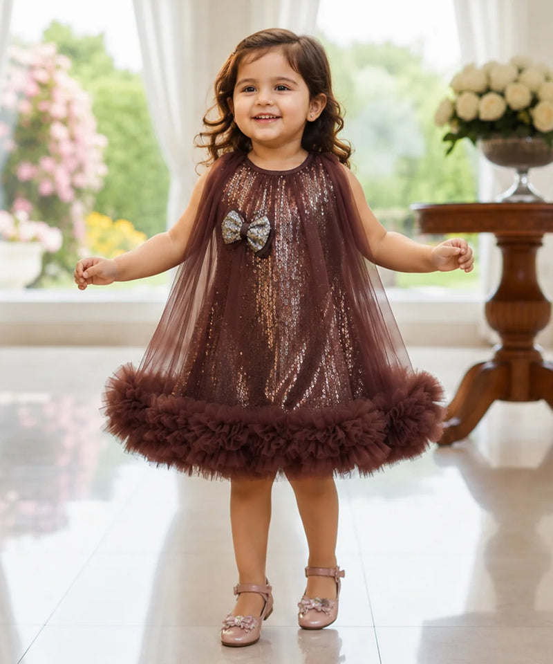 Young girl in a brown sequined dress with a fluffy skirt standing indoors.