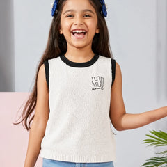 Young girl wearing a white sleeveless sweater with black trim and blue jeans, standing against a light gray background.