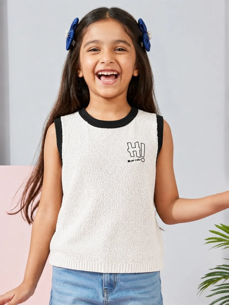 Young girl wearing a white sleeveless sweater with black trim and blue jeans, standing against a light gray background.