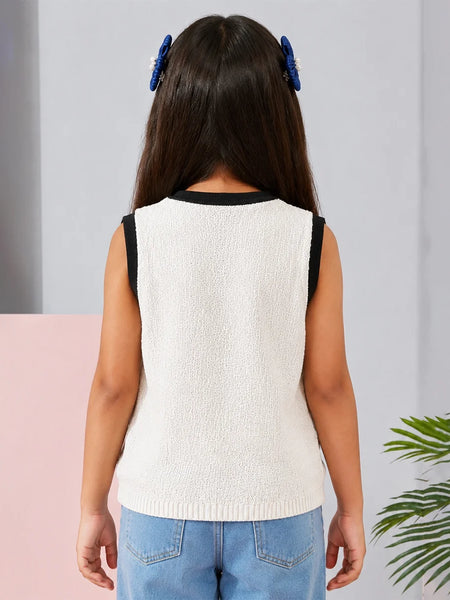 Young girl wearing a white sleeveless top with black trim and blue jeans, standing against a light gray curtain.