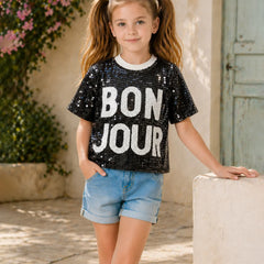 Young girl wearing a black sequin 'BON JOUR' t-shirt in an outdoor setting.