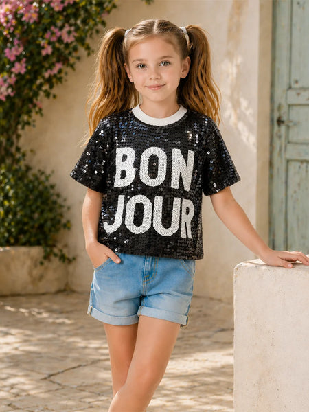 Young girl wearing a black sequin 'BON JOUR' t-shirt in an outdoor setting.