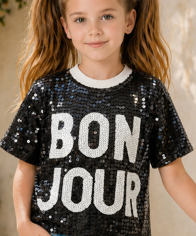 Child wearing a black sequin shirt with 'BON JOUR' text.