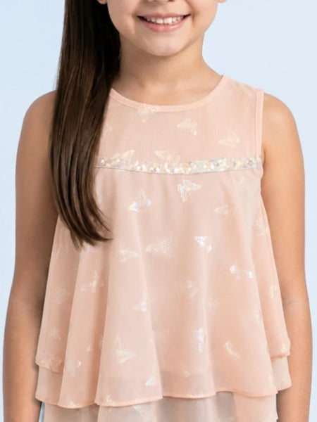 Young girl wearing a light pink sleeveless top with sequin details on a light blue background
