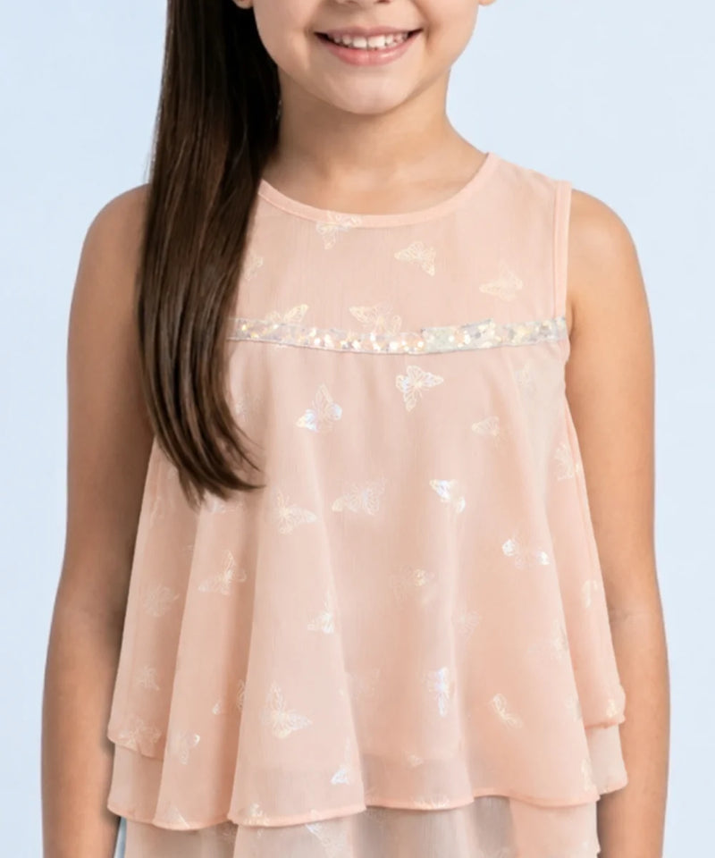 Young girl wearing a light pink sleeveless top with sequin details on a light blue background