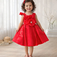 Young girl wearing a red dress with a large flower detail indoors.