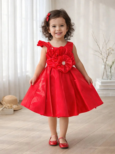 Young girl wearing a red dress with a large flower detail indoors.