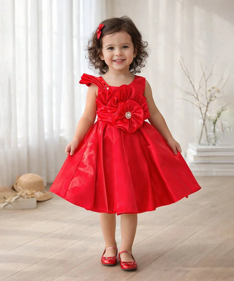 Young girl wearing a red dress with a large flower detail indoors.
