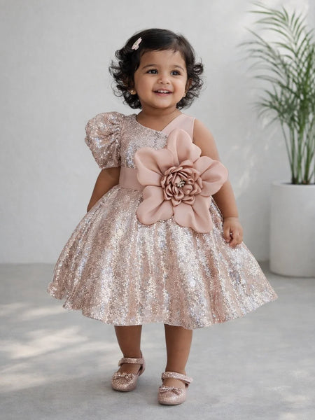 Young girl in a sparkly dress with a large pink flower standing indoors.