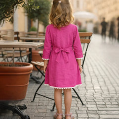 Young girl in a pink dress standing on a street with outdoor seating in the background