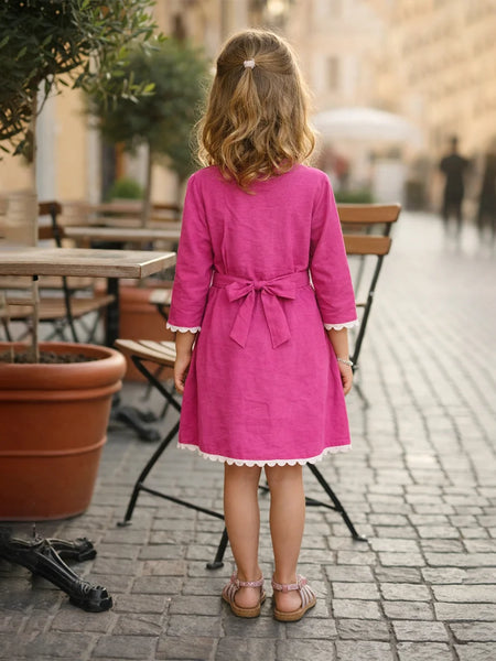 Young girl in a pink dress standing on a street with outdoor seating in the background