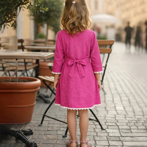 Young girl in a pink dress standing on a street with outdoor seating in the background