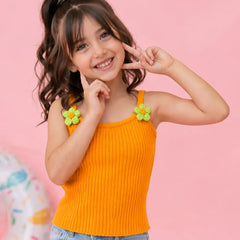 Young girl wearing an orange tank top with flower straps against a pink background
