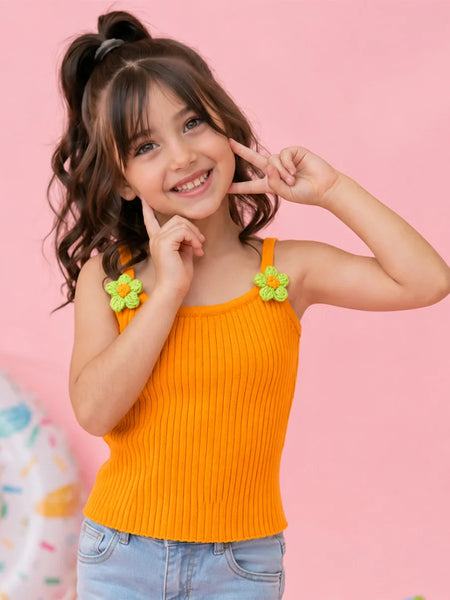 Young girl wearing an orange tank top with flower straps against a pink background