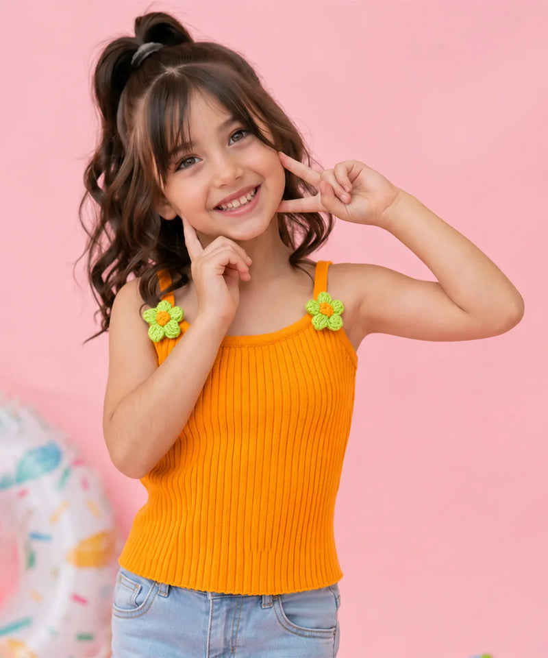 Young girl wearing an orange tank top with flower straps against a pink background