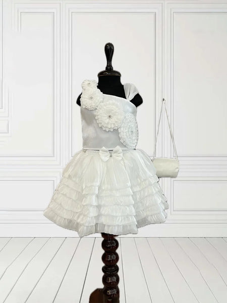 This White Coloured kids birthday wear dress consists of a crop top, a skirt and a matching handbag. It features floral detailing on the top and a cute bow on the waist.