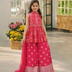 Young girl in a pink traditional outfit standing in a room with flowers and a window.