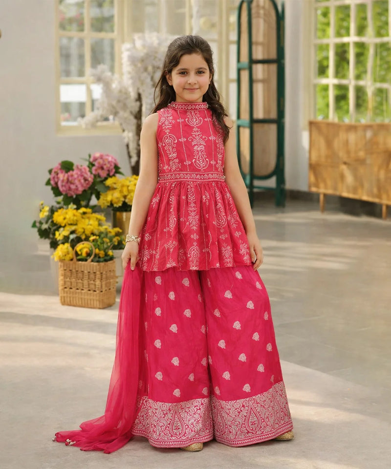 Young girl in a pink traditional outfit standing in a room with flowers and a window.