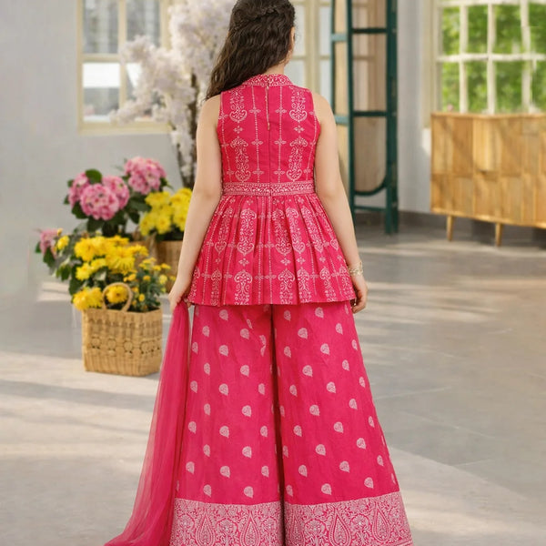 Woman wearing a pink traditional outfit with white patterns in a room with flowers and a window.