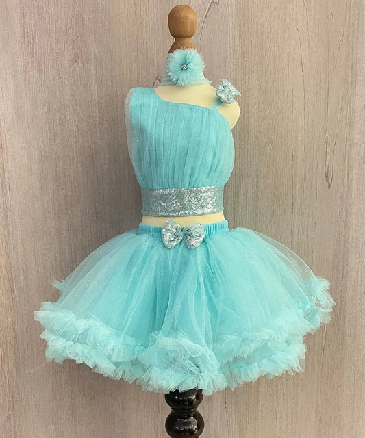 This turquoise Colored dress consists of a pleated crop-top. a skirt, a matching shoes and a hair band. It features a cute bow attached on the shoulder and on the waist. 