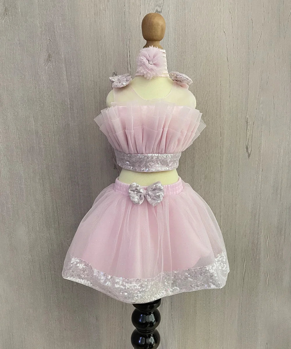It's a light pink Colored dress that consists a fancy crop-top, a skirt, a matching shoes and a hair accessory.