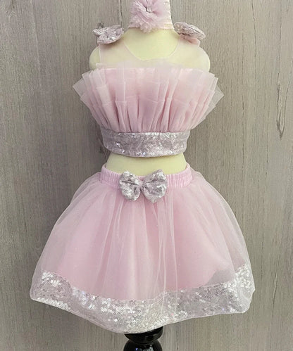 It's a light pink Colored dress that consists a fancy crop-top, a skirt, a matching shoes and a hair accessory.