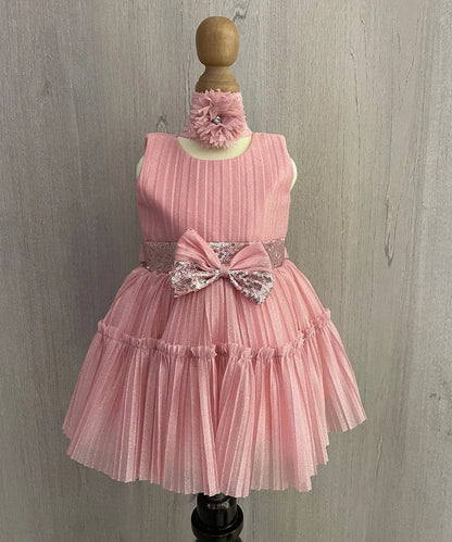 It is a pink baby girl frock with a back zip closure perfect for her birthday. It comes with a matching shoes. It features a big front bow on the waist and an attached fabric belt to be tied at the back.