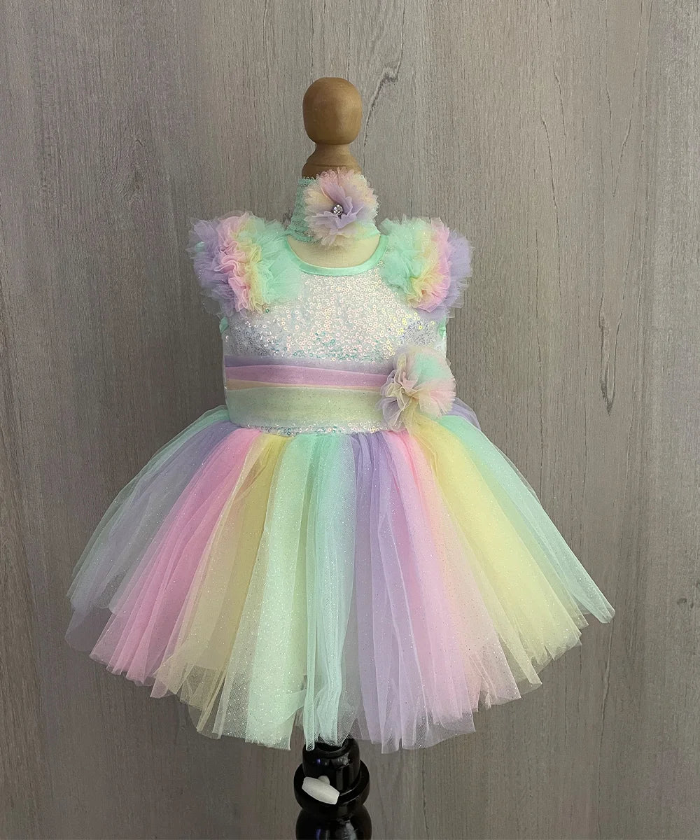  It is a multi Colored baby girl frock with a back zip closure perfect for her birthday. It comes with matching shoes and a hairband. It features flowers on the waist frill on the shoulder and an attached fabric belt to be tied at the back.