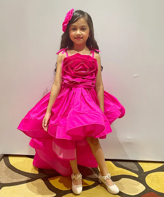 It is a designer neon pink colored up-and-down birthday girl dress that comes with a back hook closure and has a big floral detailing in the dress.