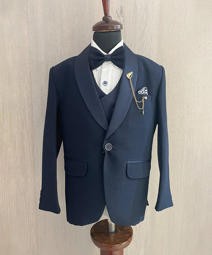 This boys wedding outfit consists of a navy Colored shimmer coat, waistcoat, matching pants and a white Colored shirt that comes with pin tucks detailing on it. It features a matching shimmer bow, a broach and a printed pocket square that uplifts the entire look.