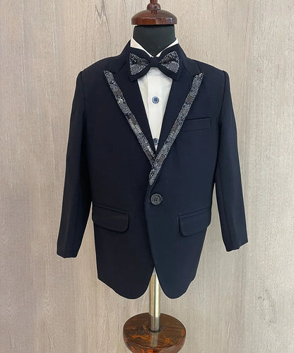 This is a navy coloured coat suit and comes with matching pants, a white shirt and a black bow. It features beautiful sequin detailing on the collar and a bow curated from a black sequin fabric