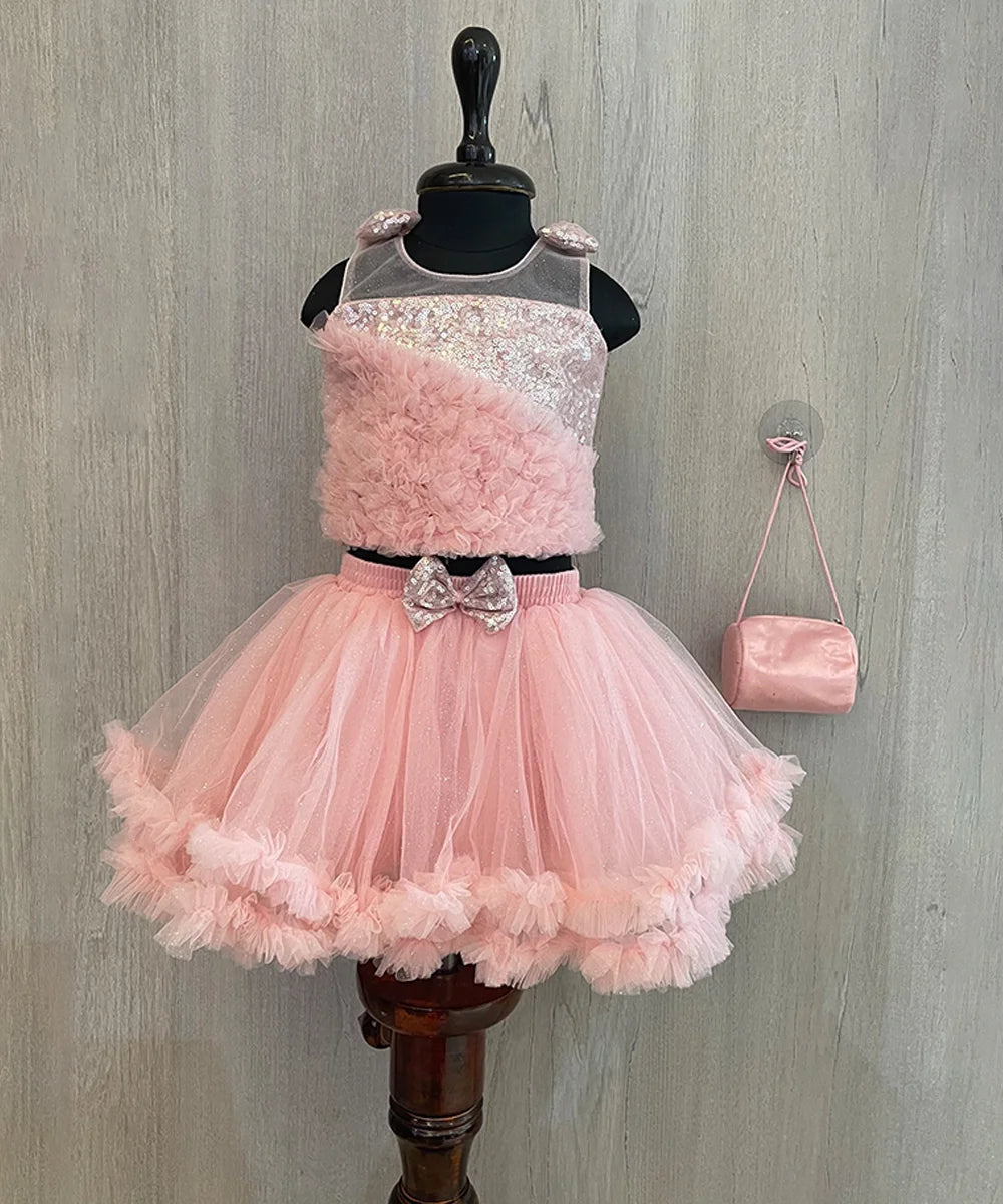 This pink colored dress consists of a fancy crop top that comes with a back hook closure and a layered ruffle skirt. It is paired up with a matching handbag, shoes and hairband. It features bow detailing on the shoulder and on the waist.