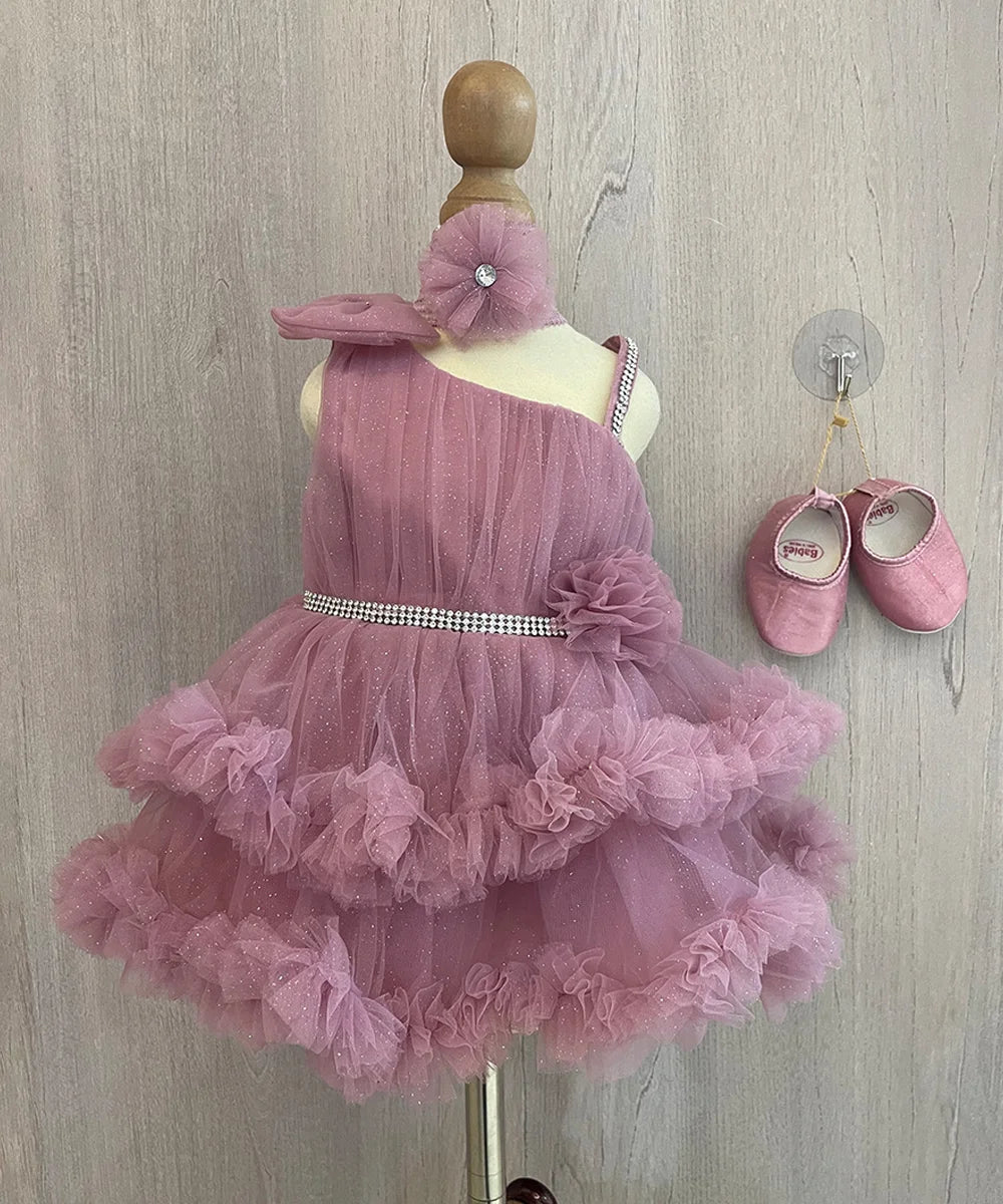 This wine Colored frock comes with a back zip closure. It is paired up with matching shoes and a hair band. It features a big bow on the shoulder and a cute flower attached with shiny lace on the waist. Moreover, it comes with a fabric belt to be tied at the back.